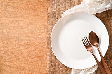Empty white plate mockup and silverware on brown place mat