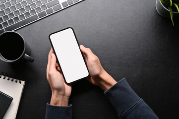 Top view, A male hands using cellphone on his dark stylish workspace.