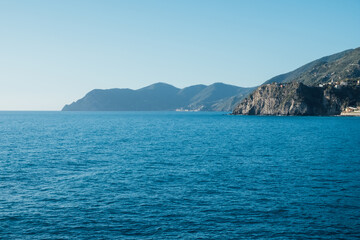 Fototapeta na wymiar Beautiful seascape with blue sky, smooth water surface and rocky cliffs in Liguria coastal area. Popular italian travel destination.