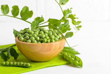 Fresh organic raw green peas in a wooden bowl with peas plants leaves on a napkin on white background. Healthy eating, vegan and vegetarian legume food, raw food and detox super food, bean protein