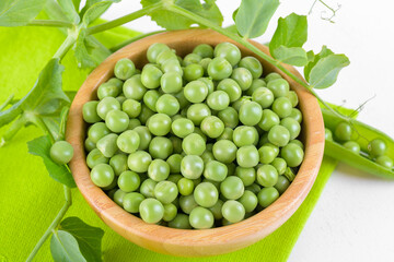 Fresh organic raw green peas in a wooden bowl with peas plants leaves on a napkin on white background. Healthy eating, vegan and vegetarian legume food, raw food and detox super food, bean protein