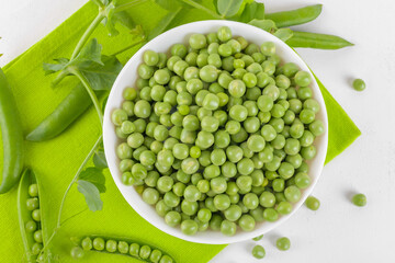 Fresh organic raw green peas in a bowl with peas plants leaves on a napkin on white background. Healthy eating, vegan and vegetarian legume food, raw food and detox super food, bean protein, top view