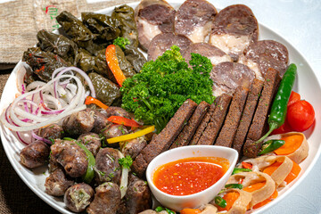 Cold cuts of sausage, grilled meat, red fish cuts, crispy bread and a cup with sauce on a large white plate.