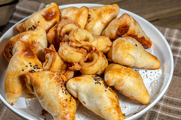 Central Asian samsa, minced meat in a dough molded into a triangle, and sweet bread on a white plate. Close-up