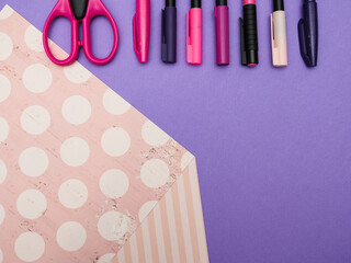 top view of different pink and purpule pens or markers and scissors on purple and pink paper background with space for text