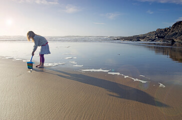 Girl (7 years old) filling bucket and spade on beach on Woolacombe beach in Devon, UK