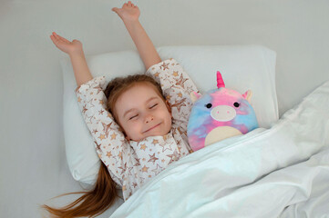 Smiling girl in pajamas stretches in bed after sleeping. Morning, earlier awakening. A sleepy child...
