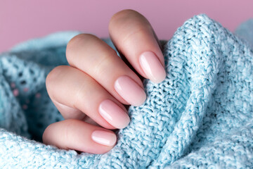 Female hand in blue knitted sweater with beautiful natural manicure - pink nude nails. Nail care...