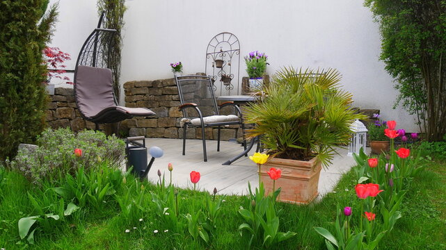 wunderschöne Gartenterrasse mit Tisch und Stühlen und einer Hängeschaukel und umgeben von diversen Pflanzen und Blumen