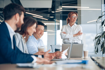 Smiling confident female boss looking at side on business meeting with colleagues in office