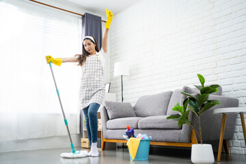 Full body portrait of a beautiful Asian woman cleaning and disinfecting all surfaces for safety reasons. She was holding a clean floor mop, wearing gloves standing in the living room in the house.