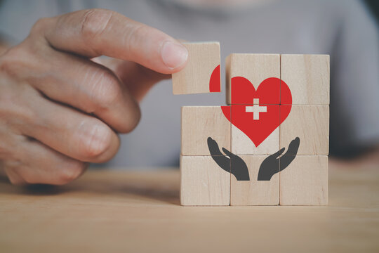 senior woman's hand hold piece of cube to complete helping hand with red heart above for life health insurance services, insurance business and healthcare concept