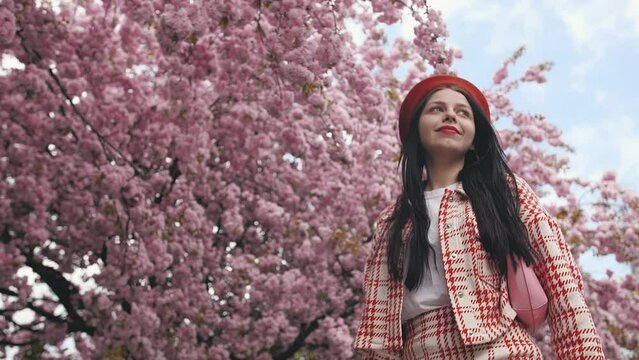 Beautiful young ukrainian girl feels free and happy look around and smiling on blurred background in the city street. Sakura tree.