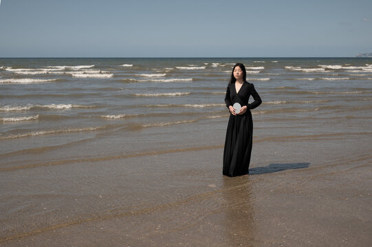 Fine art portrait of asian girl in black dress on the beach holding mirror
