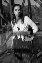 Black and white portrait of a young brunette girl in white shirt and striped trouser against city architecture