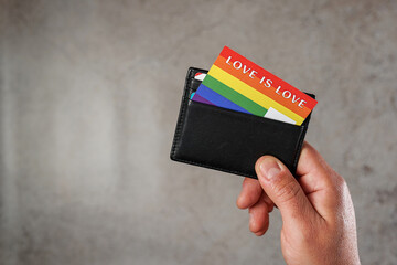 Hand of a man showing his wallet with a card with the colors of the LGBTQ movement with the phrase Love is Love. Concept of identification with the LGBTQ movement. High quality photo - obrazy, fototapety, plakaty
