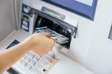 Close up of a woman's hand withdrawing cash, euro bills from the ATM bank machine. Finance customer...