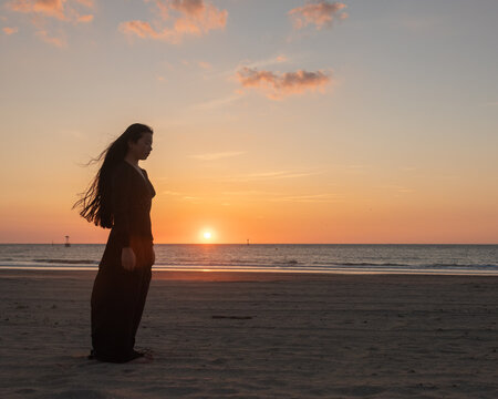silhouette of a woman in long black dress on the beach at sunset
