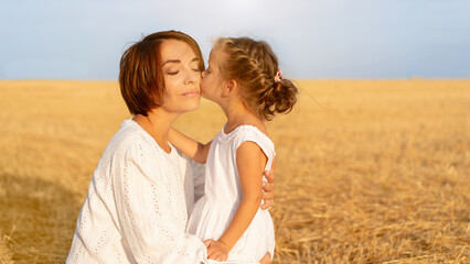 Daughter kisses her mom cheek standing wheat field