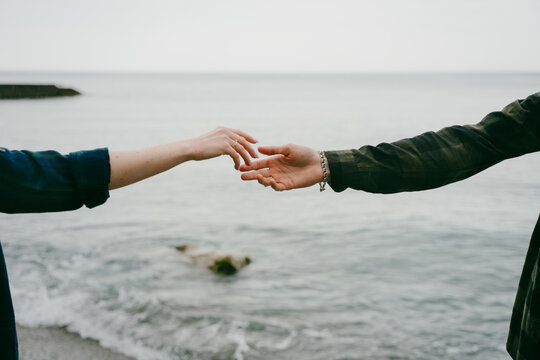 Couple stretches their arms to each other over the sea. Spring or summer holidays. The concept of family. Natural landscape. The hand of a girl and a guy reach out to each other on the seashore.
