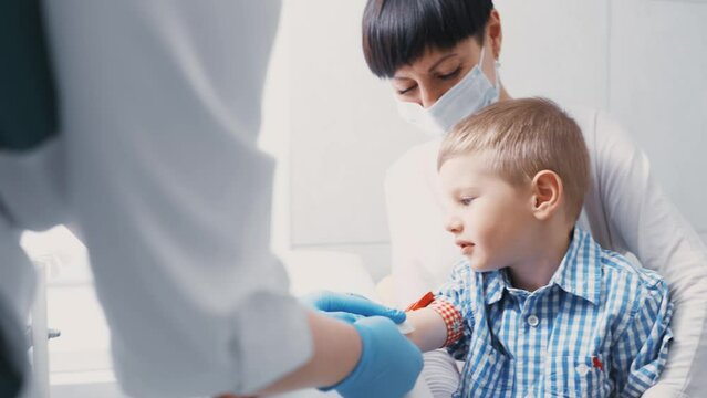 nurse gives an injection or vaccination to a little boy who is sitting in his mother's arms.