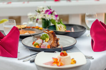 Table with fine food and drinks served for romantic dinner for couple, decorated with flowers and rose petals in luxury outdoors restaurant at hotel or resort. Summer vacations or holidays concept.