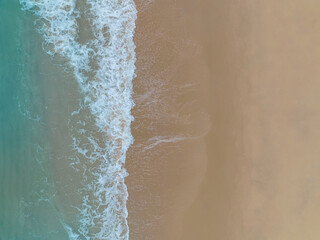 Aerial top view to tropical sandy beach and blue ocean. Top view of ocean waves reaching shore on sunn
