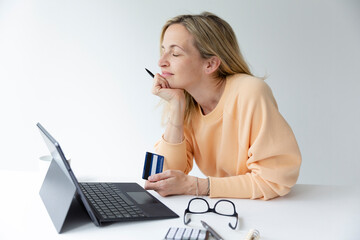 pretty young woman standing by height adjustable table ordering things over internet and enjoying online shopping with credit card