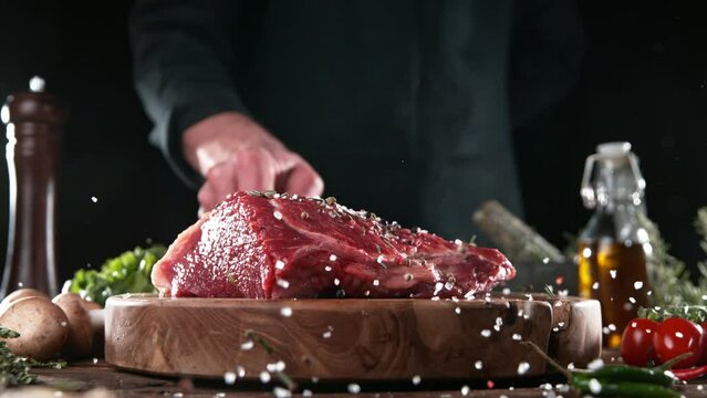 Chef throwing piece of raw beef steak on cutting board. Meat preparation in kitchen. Filmed on high speed cinema camera, 1000 fps. Speed ramp effect.