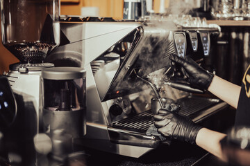 Close-up of Barista steaming milk for a hot cappuccino with a machine in a coffee shop. Process to prepare foaming milk foam for cappuccino, heating and whipping in metal Jug. Cafe Service Concept