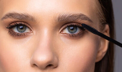 Well lit woman applying mascara to her eyelashes, Cropped image