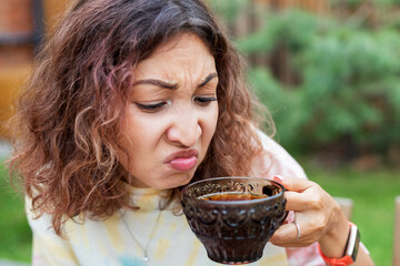 The girl tastes bitter and strong pu-erh tea or coffee and makes a disgruntled face. - obrazy, fototapety, plakaty