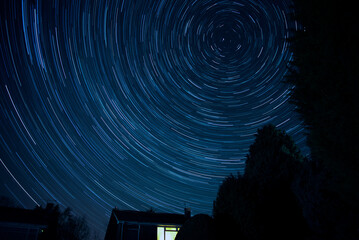 Silhouette of trees with a house under the beautiful Polaris star trails at night - Powered by Adobe