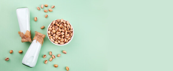 Pistachio milk in bottles and nuts on a green background. Banner. Healthy vegetarian and vegan drink, plant based milk substitute. Top view. 
