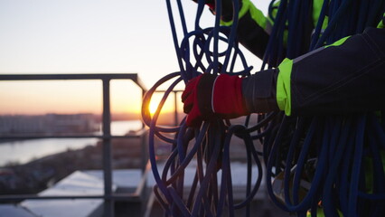 Skein of rope in hands of professional climber in special equipment. Industrial climber tries to untangle blue safety rope at sunset closeup