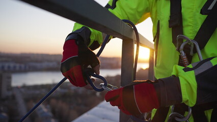 Man attaches rope with carabiner on roof steel fence. Industrial climber fastens safety equipment...