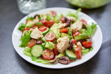 Salad with tuna, lettuce, cucumbers, tomatoes, olives and avocados in white plate on the table