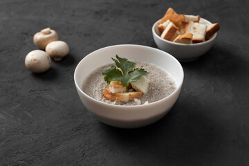 Bowl of homemade champignon mushrooms cream soup with croutons and parsley on concrete table.
