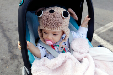Un bébé dans sa poussette avec un bonnet en forme de chien - obrazy, fototapety, plakaty