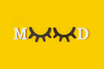Mood. White letters and wood black eyeleshes on yellow background. Creative moning concept. Top view, Flat lay. Greeting card