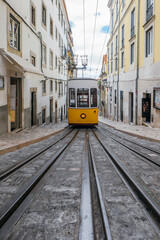 Naklejka na ściany i meble Yellow tram on the street of Lisbon, Portugal, travel destination. Trams in the city of Lisbon. Famous funicular yellow retro tram in the narrow streets of the old town of Lisbon on a sunny summer day