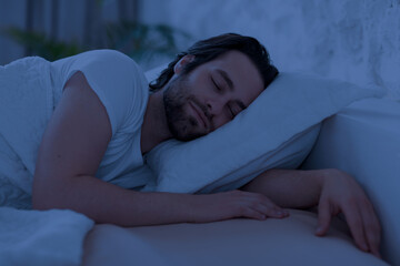 Peaceful young man sleeping in bed alone at home