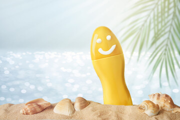 Yellow tube with happy sunscreen face on blurred sea background with palm leaves, sand and seashells