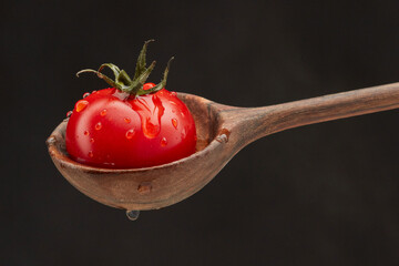 Single of tomato with water drops in a wooden spoon on a black background. Shallow depth of field