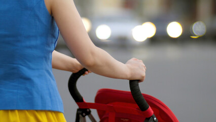 Young mother walking with baby carriage at the street back view close up. Mother with a stroller walks down the street
