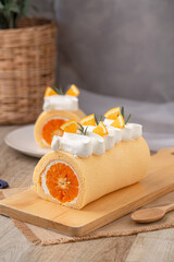 Orange roll cake topping with fresh cream orange and rosemary paste on wooden board.