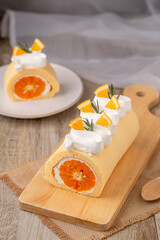 Orange roll cake topping with fresh cream orange and rosemary paste on wooden board, top view.