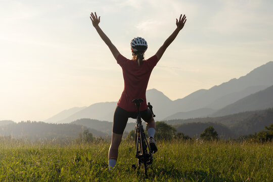 Happy female road cyclist in joy, with arms raised above her head looking at sunset