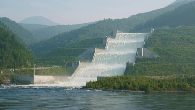 Coastal spillway of Sayano-Shushenskaya Dam on Yenisei River surrounded by forests. Passage for surplus water from hydroelectric plant. Landscape with artificial waterfall, wooded hills. Green energy