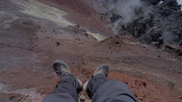 Upper view on man's feet in hiking boots at caldera of Avachinsky stratovolcano, also known as Avacha Volcano. Backpacker tourist moves upon rocks behind steam from hot geysers. Kamchatka Peninsula